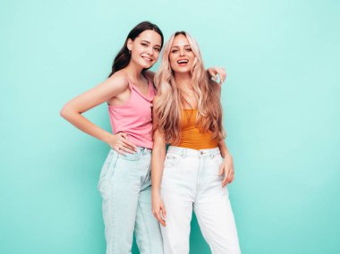 İki güzel, gülümseyen esmer hippi kadın moda yaz kıyafetleri içinde. Mavi duvarın yanında poz veren kaygısız seksi kadınlar. Pozitif modeller eğleniyor. Neşeli ve mutlu