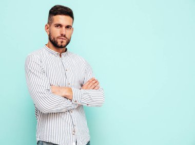 Yakışıklı, kendinden emin bir modelin portresi. Gömlek ve kot giyen seksi şık bir adam. Moda hippi erkek stüdyoda mavi duvarın yanında poz veriyor. Çapraz kollar