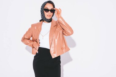 Güzel, kendine güvenen, güzel, şık elbiseli esmer bir kadın. Stüdyoda beyaz duvarın yanında poz veren kaygısız bir kadın.