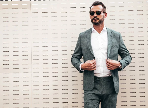 Yakışıklı, kendine güvenen, stil sahibi, lamberseksüel bir modelin portresi. Zarif takım elbise giymiş modern bir adam. Moda erkeği gün batımında Avrupa şehrinin arka planında poz veriyor. Güneş gözlükleriyle