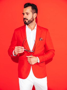 Yakışıklı, kendine güvenen hippi modelinin portresi. Zarif takım elbiseli seksi modern adam. Gözlüklü, kırmızı duvarın yanındaki stüdyoda poz veren modacı erkek.