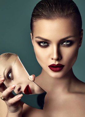 Gece makyajlı ve kırmızı dudaklı güzel esmer kadının yüksek moda portresi. Mavi arka planda kırık aynaya yansıyan kendinden emin model