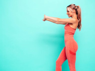 Pembe spor elbiseli, gülümseyen kadın portresi. Mükemmel vücutlu seksi genç bir manken. Stüdyoda mavi duvarın yanında poz veren bir kadın. Neşeli ve mutlu. Eğitimden önce esniyorum.