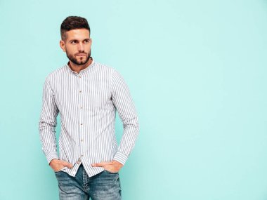 Yakışıklı, kendinden emin bir modelin portresi. Gömlek ve kot giyen seksi şık bir adam. Moda hippi erkek stüdyoda mavi duvarın yanında poz veriyor.