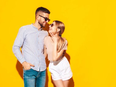 Seksi, gülümseyen güzel kadın ve yakışıklı erkek arkadaşı. Mutlu mutlu aile stüdyoda sarı duvarın yanında hassas anlar yaşıyor. Saf, neşeli modeller sarılıyor. Güneş gözlükleriyle birbirlerine sarılıyorlar.