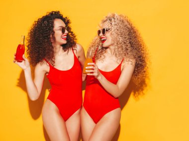 Kırmızı mayo giyen iki güzel, seksi, gülümseyen hippi kadın mayo giyiyor. Saçları kıvırcık moda modeller stüdyoda eğleniyor. Sarıda izole edilmiş seksi bir kadın.