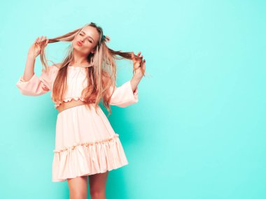 Son moda pembe elbiseler içinde gülümseyen güzel bir kadının portresi. Stüdyoda mavi duvarın yanında poz veren kaygısız sarışın kadın. Pozitif model içeride eğleniyor. Neşeli ve mutlu