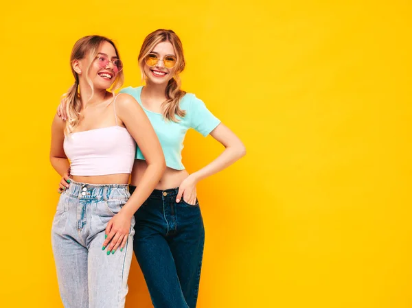 两个年轻美丽的金发嬉皮士女穿着时髦的夏装 无忧无虑的性感女人在工作室的黄墙边摆姿势 有乐趣的正面模型 快乐而快乐 戴太阳镜 — 图库照片