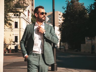 Yakışıklı, kendine güvenen, stil sahibi, Lambersex modelinin portresi. Zarif takım elbise giymiş modern bir adam. Moda erkeği gün batımında Avrupa şehrinin arka planında poz veriyor. Güneş gözlükleriyle