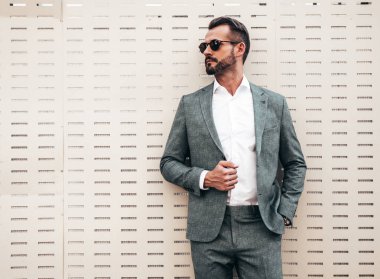Yakışıklı, kendine güvenen, stil sahibi, lamberseksüel bir modelin portresi. Zarif takım elbise giymiş modern bir adam. Moda erkeği gün batımında Avrupa şehrinin arka planında poz veriyor. Güneş gözlükleriyle