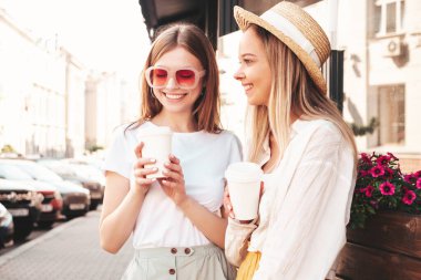 Son moda yaz kıyafetleri içinde iki güzel gülümseyen hippi kadın. Sokakta poz veren kaygısız kadınlar. Pozitif saf modeller gün batımında eğleniyorlar. Kahve ya da çay içiyorlar.