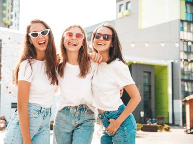 Üç güzel, gülümseyen yeniyetme kadın yazın moda olan aynı kıyafetleri giyiyor. Sokakta poz veren kaygısız seksi kadınlar. Güneş gözlükleriyle eğlenen pozitif modeller. Sarılmalar. Neşeli ve mutlu