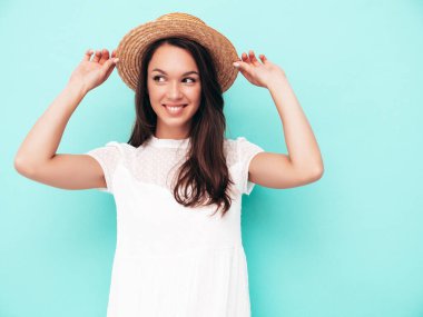 Moda kıyafetleri içinde gülümseyen güzel bir kadın. Stüdyoda mavi duvarın yanında poz veren kaygısız seksi kadın. Pozitif esmer model eğleniyor. Neşeli ve mutlu. Şapkalı.