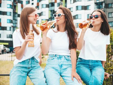 Üç güzel, güler yüzlü yeniyetme kadın aynı yaz kıyafetleri içinde. Sokakta poz veren kaygısız kadınlar. Güneş gözlükleriyle eğlenen pozitif modeller. Şişe bira içmek. Ekim Festivali