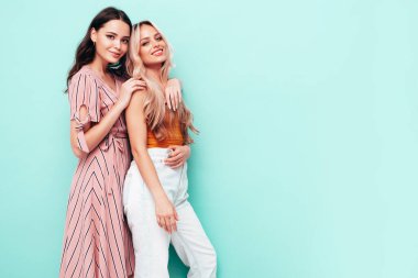 İki güzel, gülümseyen esmer hippi kadın moda yaz elbiseleri içinde. Mavi duvarın yanında poz veren kaygısız seksi kadınlar. Pozitif modeller eğleniyor. Neşeli ve mutlu