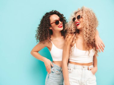 Kırmızı yaz mayo giymiş, gülümseyen iki güzel hippi kadın. Saç stili kıvırcık saçlı moda modeller stüdyoda eğleniyor. Mavide izole edilmiş seksi bir kadın. Güneş gözlükleriyle