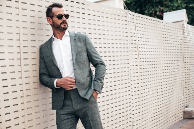 Yakışıklı, kendine güvenen, stil sahibi, Lambersex modelinin portresi. Zarif takım elbise giymiş modern bir adam. Moda erkeği gün batımında Avrupa şehrinin arka planında poz veriyor. Güneş gözlükleriyle