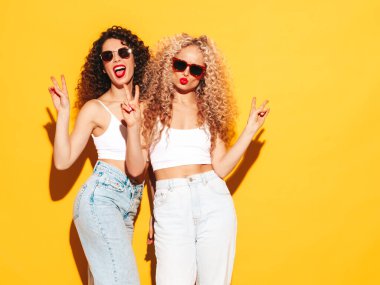 Kırmızı yaz mayo giymiş, gülümseyen iki güzel hippi kadın. Saç stili kıvırcık saçlı moda modeller stüdyoda eğleniyor. Sarıda izole edilmiş seksi bir kadın. Güneş gözlükleriyle