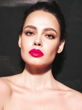 Şık makyajlı ve mükemmel temiz tenli esmer bir kadının moda portresi. Siyah duvarın yanındaki stüdyoda poz veren saçı topuzlu seksi bir manken. Pembe, doğal dudaklarıyla
