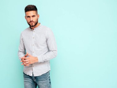 Yakışıklı, kendinden emin bir modelin portresi. Gömlek ve kot giyen seksi şık bir adam. Moda hippi erkek stüdyoda mavi duvarın yanında poz veriyor.