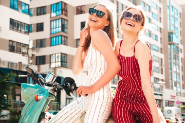 Son moda giyinmiş iki güzel, gülümseyen yeniyetme kadın. Sokakta geçmişe dönük motosiklet süren kaygısız kadınlar. Eğlenceli ve klasik İtalyan mobiletleriyle gezen pozitif modeller.