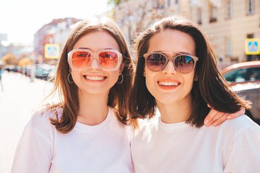 Son moda yaz kıyafetleri içinde iki güzel gülümseyen hippi kadın. Sokakta poz veren kaygısız kadınlar. Pozitif saf modeller gün batımında eğleniyor, sarılıyor ve deliriyor. Mutlu ve neşeli.