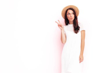 Moda kıyafetleri içinde gülümseyen güzel bir kadın. Stüdyoda pembe duvarın yanında poz veren kaygısız bir kadın. Pozitif esmer model eğleniyor. Neşeli ve mutlu. Şapkalı. Barış işareti gösterir