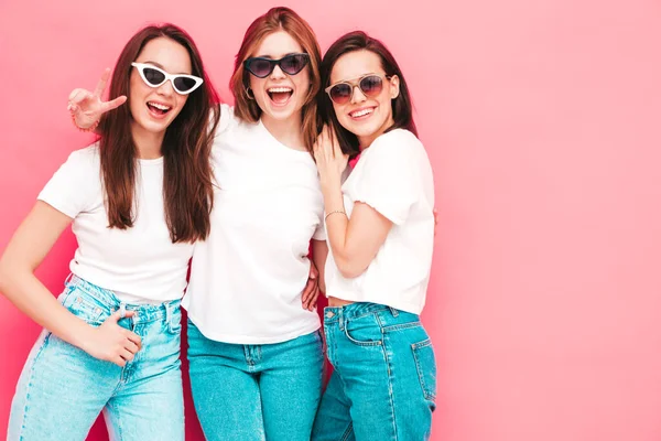 同じ夏の白いTシャツとジーンズの服で流行の3人の若い美しい笑顔のヒップスター女性 スタジオでピンクの壁の近くにポーズをとるセクシーな屈託のない女性 正のモデル — ストック写真