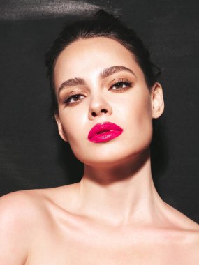 Şık makyajlı ve mükemmel temiz tenli esmer bir kadının moda portresi. Siyah duvarın yanındaki stüdyoda poz veren saçı topuzlu seksi bir manken. Pembe, doğal dudaklarıyla