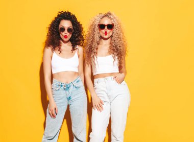 Yaz kıyafetleri içinde gülümseyen iki güzel hippi kadın. Stüdyoda afro kıvırcık saçlı moda modeller var. Sarıda izole edilmiş seksi bir kadın. Mutlu ve neşeli. Güneş gözlüklü. Ördek suratları yapmak
