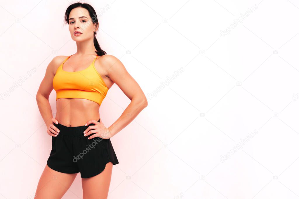 Fitness confident woman in sports clothing. Sexy young beautiful model with perfect body. Female posing near wall in studio. Stretching out before training