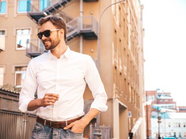 Yakışıklı, gülümseyen stil sahibi Lambersex modelinin portresi. Beyaz gömlek giymiş modern bir adam. Moda erkeği sokakta poz veriyor. Gün batımında dışarıda.