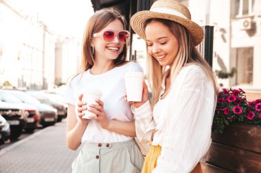 Son moda yaz kıyafetleri içinde iki güzel gülümseyen hippi kadın. Sokakta poz veren kaygısız kadınlar. Pozitif saf modeller gün batımında eğleniyorlar. Kahve ya da çay içiyorlar.