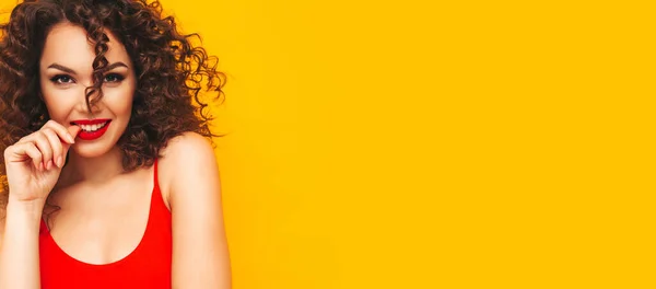 流行の夏服の若い美しい笑顔ブロンドのヒップスター女性の肖像画 スタジオでアフロカールの髪型でポーズをとるセクシーな屈託のない女性 正のモデルは指をかむ 黄色に隔離された — ストック写真