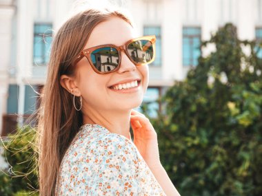 Moda kıyafetleri içinde gülümseyen genç ve güzel bir hippi kadın. Günbatımında sokakta poz veren kaygısız seksi kadın. Açık havada pozitif model. Neşeli ve mutlu güneş gözlükleriyle
