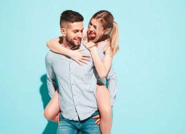 Seksi, gülümseyen güzel kadın ve yakışıklı erkek arkadaşı. Mutlu mutlu aile stüdyoda mavi duvarın yanında hassas anlar yaşıyor. Saf, neşeli mankenler sarılıyor. Sırtına biniyor. 