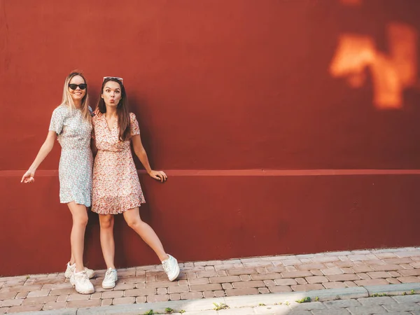 流行の夏のドレスで2人の若い美しい笑顔ヒップスター女性 Sexy屈託のない女性が赤い壁の近くの通りの背景にポーズ 正の純粋なモデルは 日没で楽しみを持っています — ストック写真