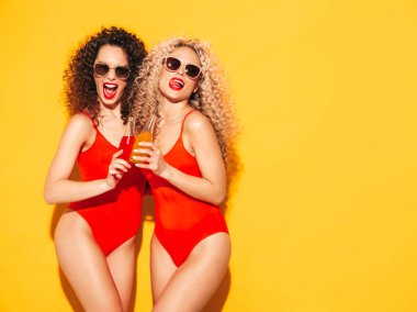 Kırmızı mayo giyen iki güzel, seksi, gülümseyen hippi kadın mayo giyiyor. Saçları kıvırcık moda modeller stüdyoda eğleniyor. Sarıda izole edilmiş seksi bir kadın.