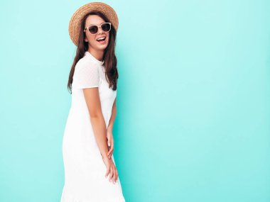 Moda kıyafetleri içinde gülümseyen güzel bir kadın. Stüdyoda mavi duvarın yanında poz veren kaygısız seksi kadın. Pozitif esmer model eğleniyor. Neşeli ve mutlu. Şapkalı.