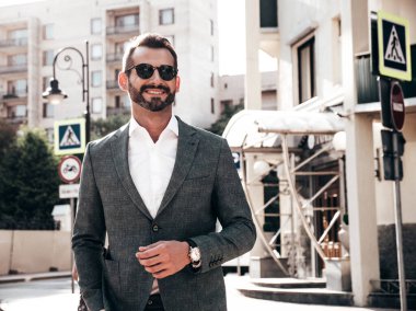 Yakışıklı, kendine güvenen, stil sahibi, Lambersex modelinin portresi. Zarif takım elbise giymiş modern bir adam. Moda erkeği gün batımında Avrupa şehrinin arka planında poz veriyor. Güneş gözlükleriyle