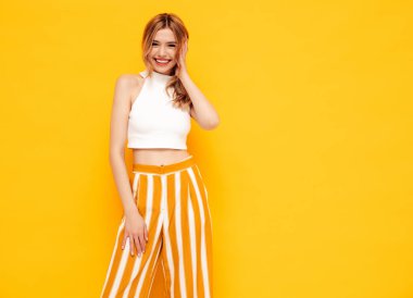 Moda kıyafetleri içinde gülümseyen sarışın güzel bir kadının portresi. Stüdyoda sarı duvarın yanında poz veren kaygısız bir kadın. Pozitif model içeride eğleniyor. Neşeli ve mutlu