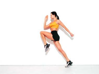 Seksi spor elbiseli spor kadını. Mükemmel vücutlu genç ve güzel bir model. Güneşli yaz gününde beyaz duvarın yanındaki stüdyoda poz veren bir kadın. Zıpla ve koş.