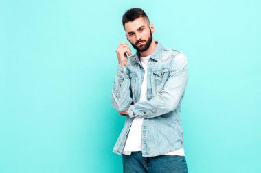 Yakışıklı, kendine güvenen, stil sahibi, Lambersexual modelin portresi. Ceket ve kot giyen adam. Moda erkeği stüdyoda mavi duvarın yanında poz veriyor.