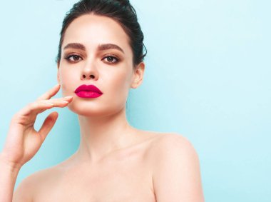 Şık makyajlı ve mükemmel temiz tenli esmer bir kadının moda portresi. Mavi duvarın yanındaki stüdyoda poz veren saçı topuzlu seksi bir manken. Pembe, doğal dudaklarıyla