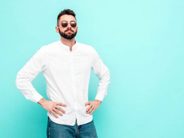 Yakışıklı, kendine güvenen, stil sahibi, Lambersex mankeni portresi. Beyaz gömlek ve kot giyen adam. Moda erkeği stüdyodaki mavi duvarda izole edilmiş. Güneş gözlükleriyle