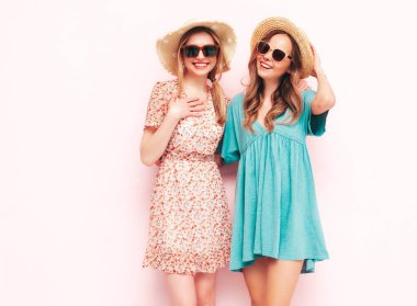 İki güzel, gülümseyen esmer hippi kadın moda yaz elbiseleri içinde. Pembe duvarın yanında poz veren kaygısız seksi kadınlar. Pozitif modeller eğleniyor. Neşeli ve mutlu. Şapka ve güneş gözlükleriyle