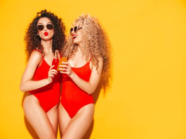 Kırmızı mayo giyen iki güzel, seksi, gülümseyen hippi kadın mayo giyiyor. Saçları kıvırcık moda modeller stüdyoda eğleniyor. Sarıda izole edilmiş seksi bir kadın.