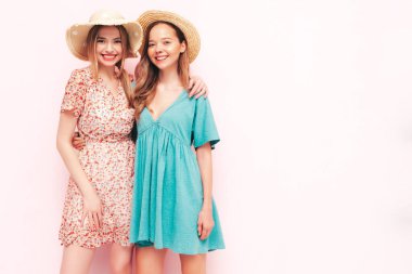İki güzel, gülümseyen esmer hippi kadın moda yaz elbiseleri içinde. Pembe duvarın yanında poz veren kaygısız seksi kadınlar. Pozitif modeller eğleniyor. Neşeli ve mutlu. Şapkalı. 