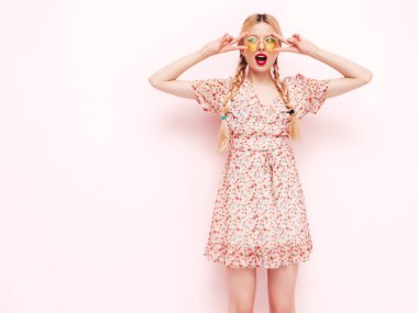 Son moda kırmızı elbisesi içinde gülümseyen güzel bir kadın. Stüdyoda duvarın yanında poz veren kaygısız sarışın kadın. Pozitif model eğleniyor. Güneş gözlükleriyle neşeli ve mutlu. İzole edilmiş