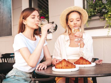 Son moda yaz kıyafetleri içinde iki güzel gülümseyen yeniyetme kadın. Sokakta Veranda Kafe 'de poz veren kaygısız kadınlar. Beyaz şarap içen pozitifler.